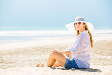 Fototapeta na wymiar Beautifil young woman sitting on the beach at sunny day enjoing