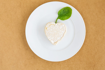 сыр в форме сердца с побегом шпината на белой тарелке сверху