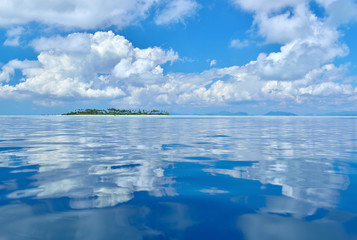 Reflection of clouds on calm and tranquil ocean with island in the distance, Sabah Borneo, Malaysia.