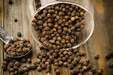 Black pepper in the glass on wooden background, food seasoning