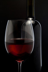 Red wine glass and a bottle in black background