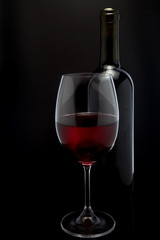 Red wine glass and a bottle in black background