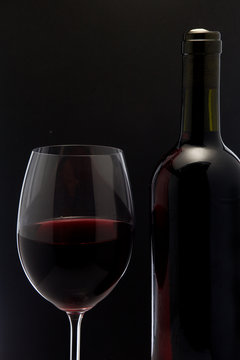 Red wine glass and a bottle in black background
