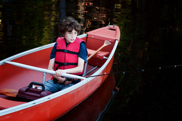 boy wearing a lifejacket fishing in a canoe