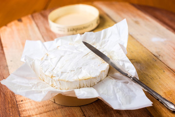 Camembert cheese wrapped in paper with vintage knife on wooden table