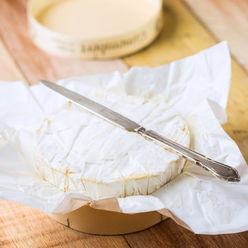 Camembert cheese wrapped in paper with vintage knife on wooden t