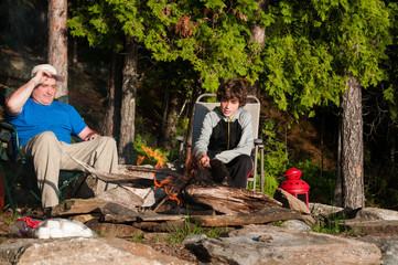 father and son sitting by a campfire roasting marshmallows