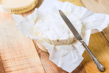 Fototapeta na wymiar Camembert cheese wrapped in paper with vintage knife on wooden t