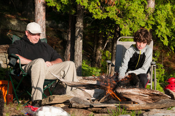 father and son sitting by a campfire roasting marshmallows