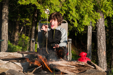 boy sitting by a campfire roasting marshmallows