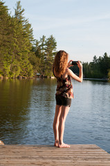 teen girl using her phone to take a photograph of a lake