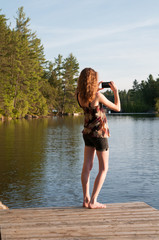 teen girl using her phone to take a photograph of a lake