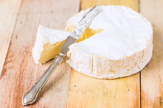 Camembert cheese wrapped in paper with vintage knife on wooden table