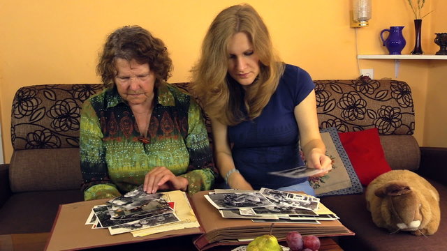 Happy senior woman with granddaughter watch photos in old album