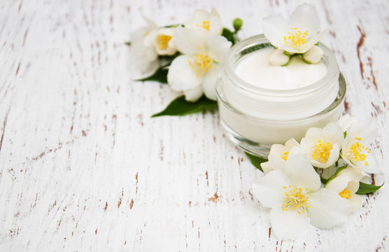 face and body cream moisturizers with jasmine flowers on white wooden background
