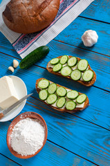 Freshly baked bread, floar, sandwich with sliced cucumbers and butter on dish in rural or rustic kitchen at vintage wood table from above.