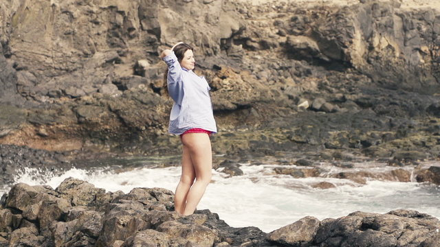 Happy woman in mens shirt enjoying herself standing on rocks near sea, slow motion shot at 240fps 
