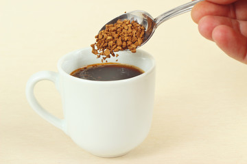 Hand pours granulated coffee from a spoon in a coffee cup