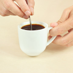 Hands mixing with a spoon of black coffee in the cup