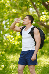 Active man drinking water from a bottle, outdoor. Young muscular male quenches thirst
