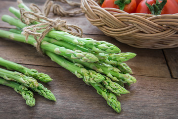 Bunch of asparagus on wooden table and tomato in basket