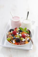 fruit salad and various yoghurt on white wooden table, vertical