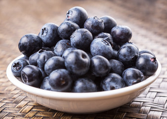 Blueberry fruits in a white bowl over wicker background