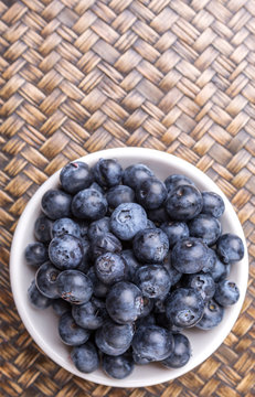 Blueberry fruits in a white bowl over wicker background