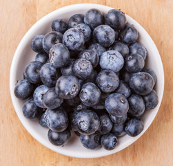 Blueberry fruits in a white bowl on wooden board background