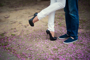 Beautiful legs of young girl in high heels next to the legs Man in pink flower petals, style, fashion, concept, romance