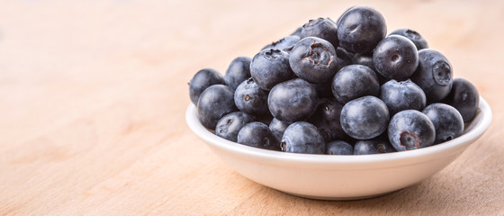 Blueberry fruits in a white bowl on wooden board background