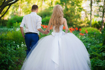 The bride and groom are in the park holding hands around the beautiful flower beds of poppies and...