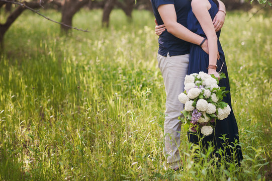Young couple with a big bouquet of flowers is goes, embracing in nature