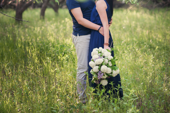 Young couple with a big bouquet of flowers is goes, embracing in nature