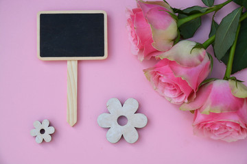 Pink painted wooden background with empty black chalk board and pink roses and flower decoration