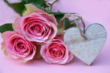 pink painted wooden background with bunch of pink roses and a heart shape photo frame decorated with white wash flowers