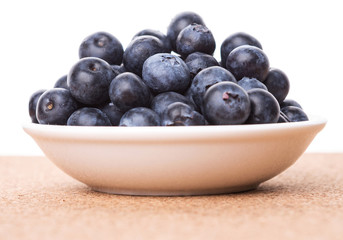 Blueberry in a white bowl on cork board background