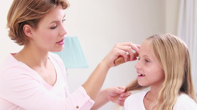 Smiling mother combing hair of daughter