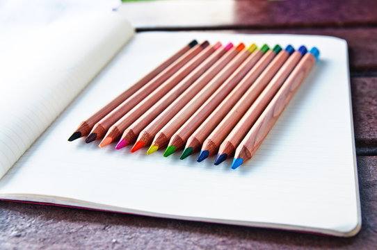 Colored pencils lined up in a row on a blank page in a notebook
