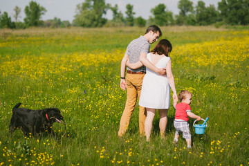 Happy family walking with black labrador dog in summer field