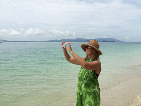 Woman taking a photo on the beach using a mobile device