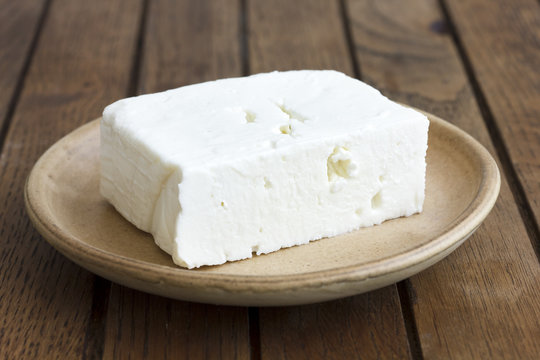 Greek feta cheese block on rustic plate and table.