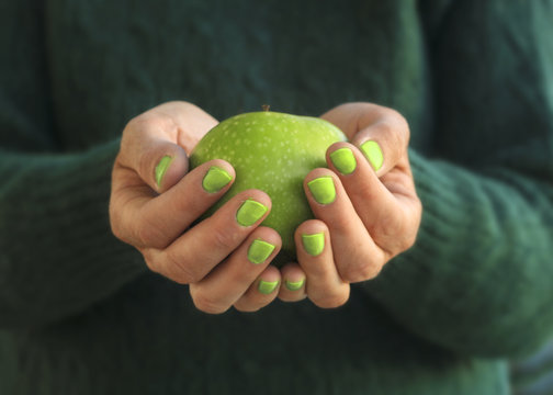 Close-up of a woman with green nail polish holding a green apple in the palm of her hands