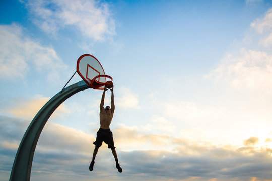 Man dunking basketball into hoop against cloudy sky&dagger;