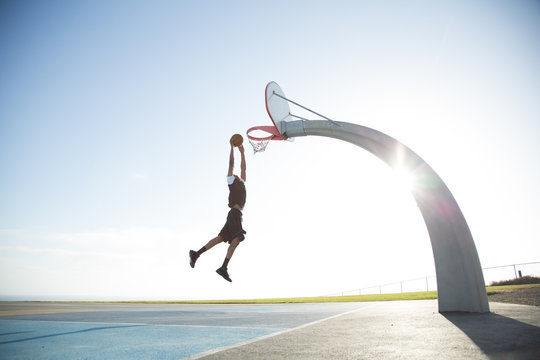 Man dunking basketball into hoop against clear sky&dagger;