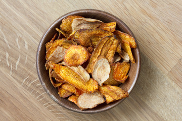 Fried carrot and parsnip chips in rustic wood bowl. From above.