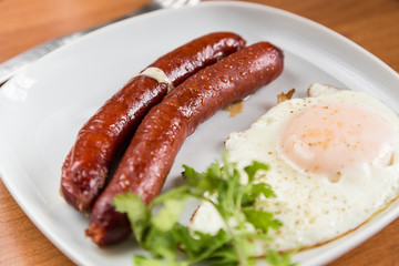 Sausage and fried egg on white plate at table