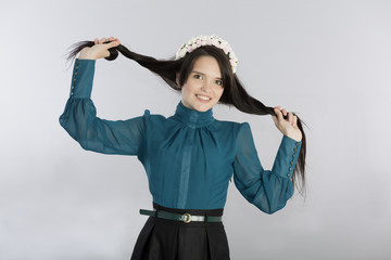 Cute young woman making hair style.
Beautiful girl classic style dressed black skirt and green tunic keeping strands of hair with vintage hair garland of flowers on top of her head on grey background