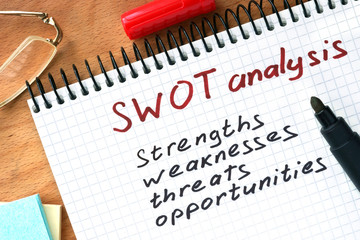 Notepad with  SWOT analysis concept on a wooden board.
