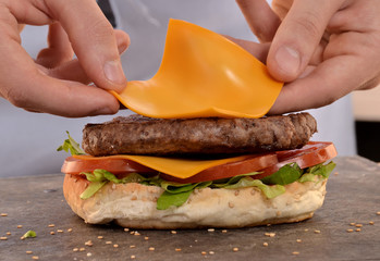 Cocinero preparando hamburguesa de queso,agregando ingredientes.